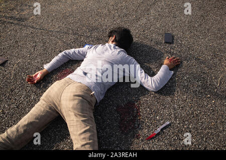 Concept of Crime or murder scene, Closeup of victim dead body murdered with knife laying on Roadside Stock Photo