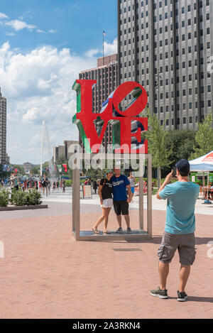 Love couple, view of a smiling young man and woman being photographed under the famous LOVE sculpture in JFK Plaza, Philadelphia,Pennsylvania, PA, USA Stock Photo