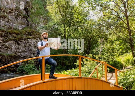 Adventure man with map and backpack on mountain in sun day. Bearded man tourist in mountain read the map. Stock Photo