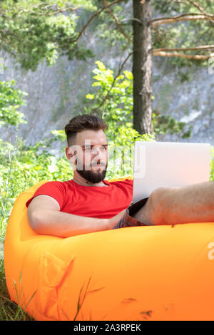 male freelancer working on computer. Young man using a laptop outdoors. Student learning or entrepreneur working with a laptop in camping. Stock Photo