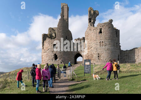A group of visitors outside the gatehouse of Dunstanburgh castle, Northumberland, England, UK Stock Photo
