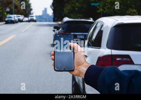 A man's hand holding a cell phone with the the words rideshare on the screen in front of a row of cars. Stock Photo