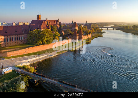 Medieval Malbork (Marienburg) Castle in Poland, main fortress of the Teutonic Knights at the Nogat river, bridges and a water scooter. Aerial view Stock Photo