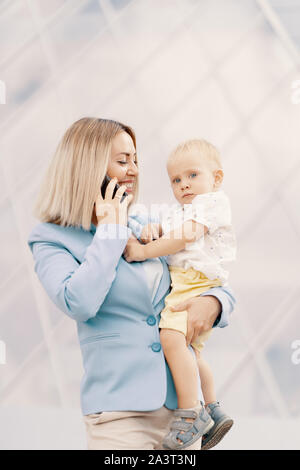Successful business woman in blue suit with baby. Successful mother in business walking with baby in her hands and talking on cellphone Stock Photo