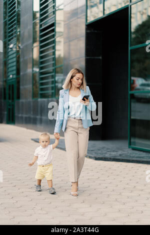 Successful business woman in blue suit with baby. Successful mother in business walking with baby and texting message on cellphone Stock Photo
