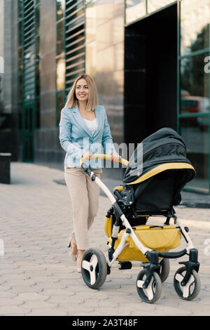 Portrait of a successful business woman in blue suit with baby. Business woman pushing baby stroller Stock Photo