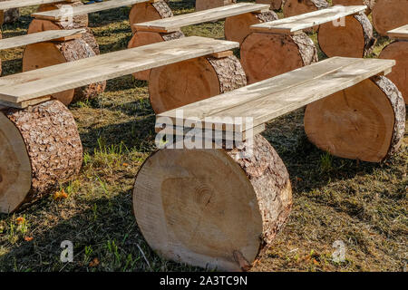 Several benches from wooden boards, standing on round saw cuts from pine logs. Raw rough tree. Country style Stock Photo
