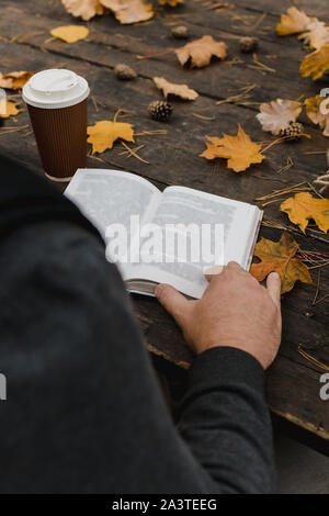 male female reads a book in autumn park drinks takeaway coffee coffee. Close-up over shoulder, blurred. top view, save space. Seen hands. In a dark Stock Photo
