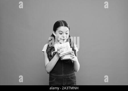 It caught her by surprise. Cute small child opening gift box with surprise face on orange background. Adorable little girl getting birthday surprise. Being shocked of pleasant surprise. Stock Photo