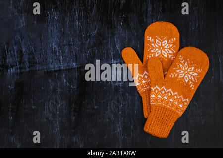 a pair of yellow orange knitted mittens on a dark blue-green-brown wooden Stock Photo