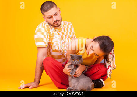 Boyfriend looking how his beautiful girlfriend's playing with their cat. Happy cat with her owners. Stock Photo