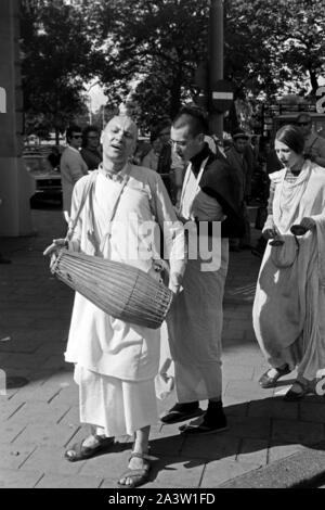 Singend, lobpreisend und trommelnd bewegen sich Hare Krishna Jünger durch die Straßen von Amsterdam, Niederlande 1971. Singing, praising and drumming Hare Krisha followers dancing through the streets of Amsterdam, The Netherlands 1971. Stock Photo