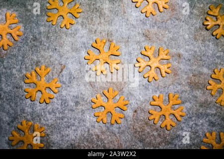 gingerbread cookie cut in the form of a snowflake made from raw dough on parchment baking paper on a dark background. View from above. save space Stock Photo