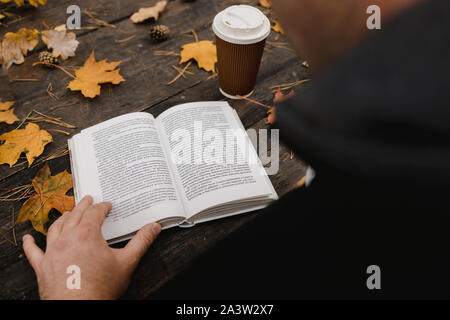male female reads a book in autumn park drinks takeaway coffee coffee. Close-up over shoulder, blurred. top view, save space. Seen hands. In a dark Stock Photo