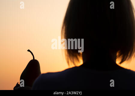 Woman with pear in hand at sunset, autumn sunset, woman silhouette Stock Photo