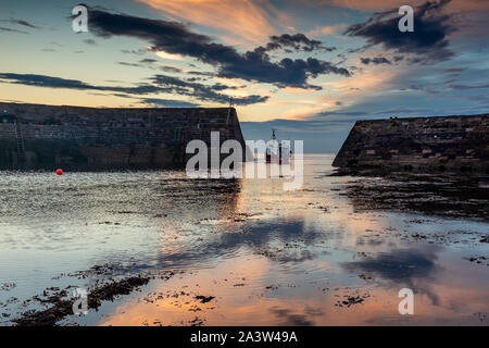 Fishing boat leaving the picturesque harbour at Cove, near Cockburnspath in Berwickshire , Scottish Borders, Scotland ,UK Stock Photo