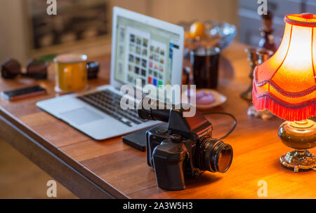 A view of a home office with a medium format analog camera on a table in front of a laptop and other various objects. Stock Photo