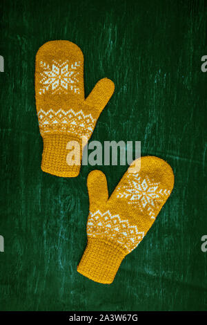 a pair of yellow orange knitted mittens on a dark blue-green-brown wooden Stock Photo