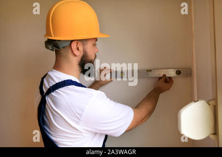Construction worker is working on renovation of apartment. Builder is measuring and checking wall room using leveler tool and spirit level tool. Stock Photo