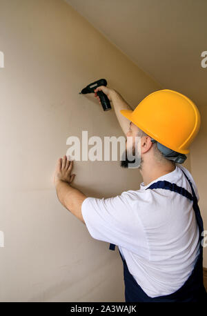 Construction worker and handyman works on renovation of apartment. Builder using electric screwdriver and screwing screw out of wall. Stock Photo
