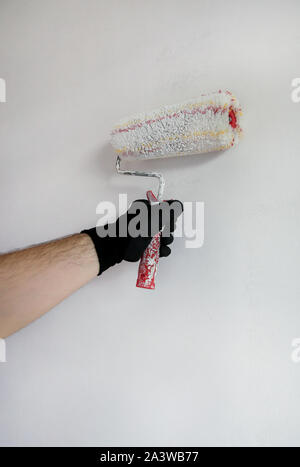 Construction worker doing finish renovation at apartment. Professional painter contractor using white paint roller brush painting of concrete wall. Stock Photo