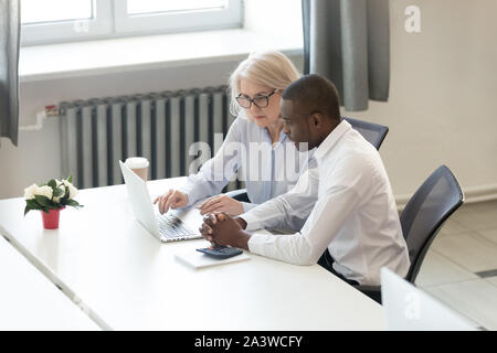 Concentrated diverse employees sitting at desk working using laptop Stock Photo