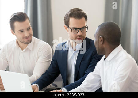 Multiracial employees businessmen working together sitting at desk use pc Stock Photo