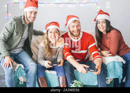 Happy couple of friends playing video games during christmas time at home - Young people having fun with new trends technologies console online Stock Photo