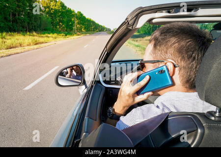 guy behind wheel of car talking on phone and looking at road with an anxious look. Unsafe driving the car. Talking on the phone behind the wheel. busi Stock Photo