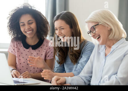 Funny diverse colleagues sitting at desk laughing received humorous video Stock Photo