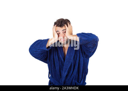 Portrait of tardy young man wears blue bathrobe holding hands to head, unable to wake up in time to get to work, isolated on white background. Stock Photo