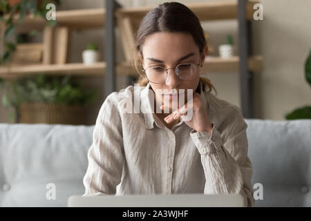 Focused thoughtful female freelancer working on laptop at home Stock Photo