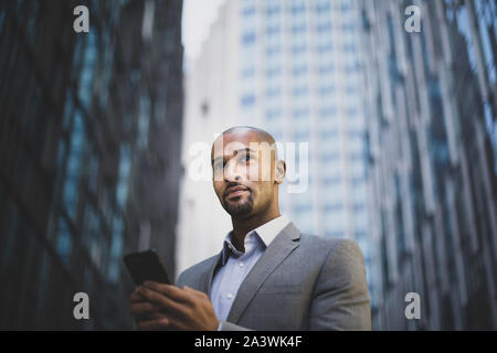 Businessman walking in city using smartphone Stock Photo
