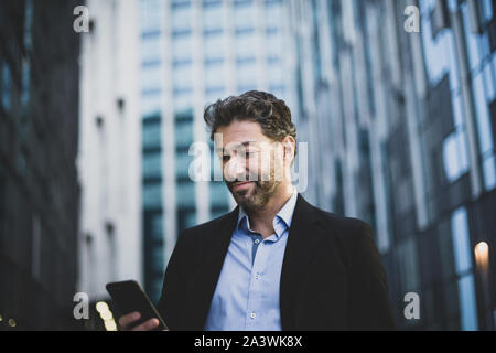 Businessman walking in city using smartphone Stock Photo