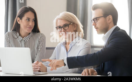 Businesspeople gather together in office sitting at desk using laptop Stock Photo