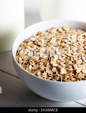 Rolled oats or oat flakes in bowl with bottle of milk on white background Stock Photo
