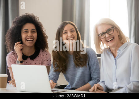 Women different ethnicity and ages looking away laughing at workplace Stock Photo