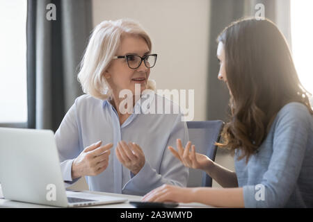Different ages employees sitting at desk working together discussing project Stock Photo