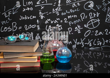 Glasses on old books and experiment bottle on a black table with a blackboard on the background. Stock Photo
