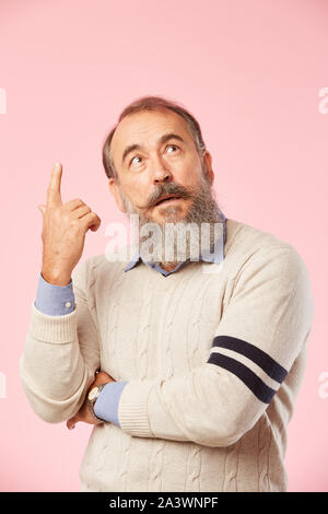 Portrait of senior man with grey beard has a god idea he standing and pointing upwards isolated on pink background Stock Photo