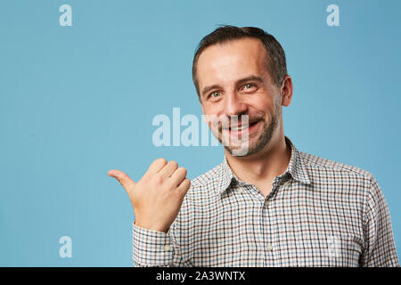 Portrait of young man with stubble showing the direction and smiling at camera over blue background Stock Photo
