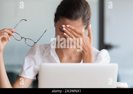 Stressed tired young business woman holding glasses feeling headache Stock Photo