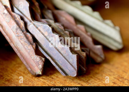 Close up of the blades of several pin tumbler style keys, some old and rusty, against a plain brown wooden background. Stock Photo