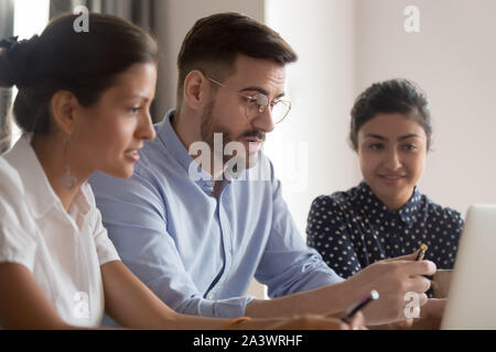 Serious caucasian teacher instructing diverse students explaining computer project Stock Photo