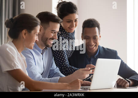 Smiling diverse ethnicity employees group gather looking pointing at laptop Stock Photo