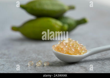 Spoon with fresh raw finger lime caviar close up and whole fruits at the background Stock Photo