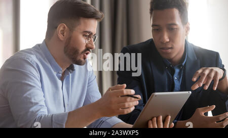 Serious african and caucasian coworkers using digital tablet discussing strategy Stock Photo
