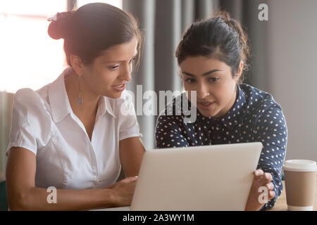 Focused diverse ethnicity female coworkers team brainstorming pointing on laptop Stock Photo