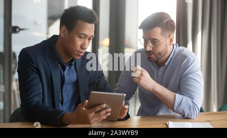 Focused black and white partners discussing project using digital tablet Stock Photo