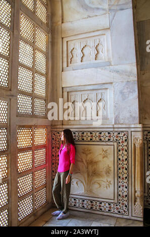 Young woman standing by lattice jali screen inside Taj Mahal, Agra, Uttar Pradesh, India. It was built in 1632 by the Mughal emperor Shah Jahan to hou Stock Photo